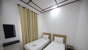 A hotel room with two single beds, a small shelf, a door, and a patterned rug.