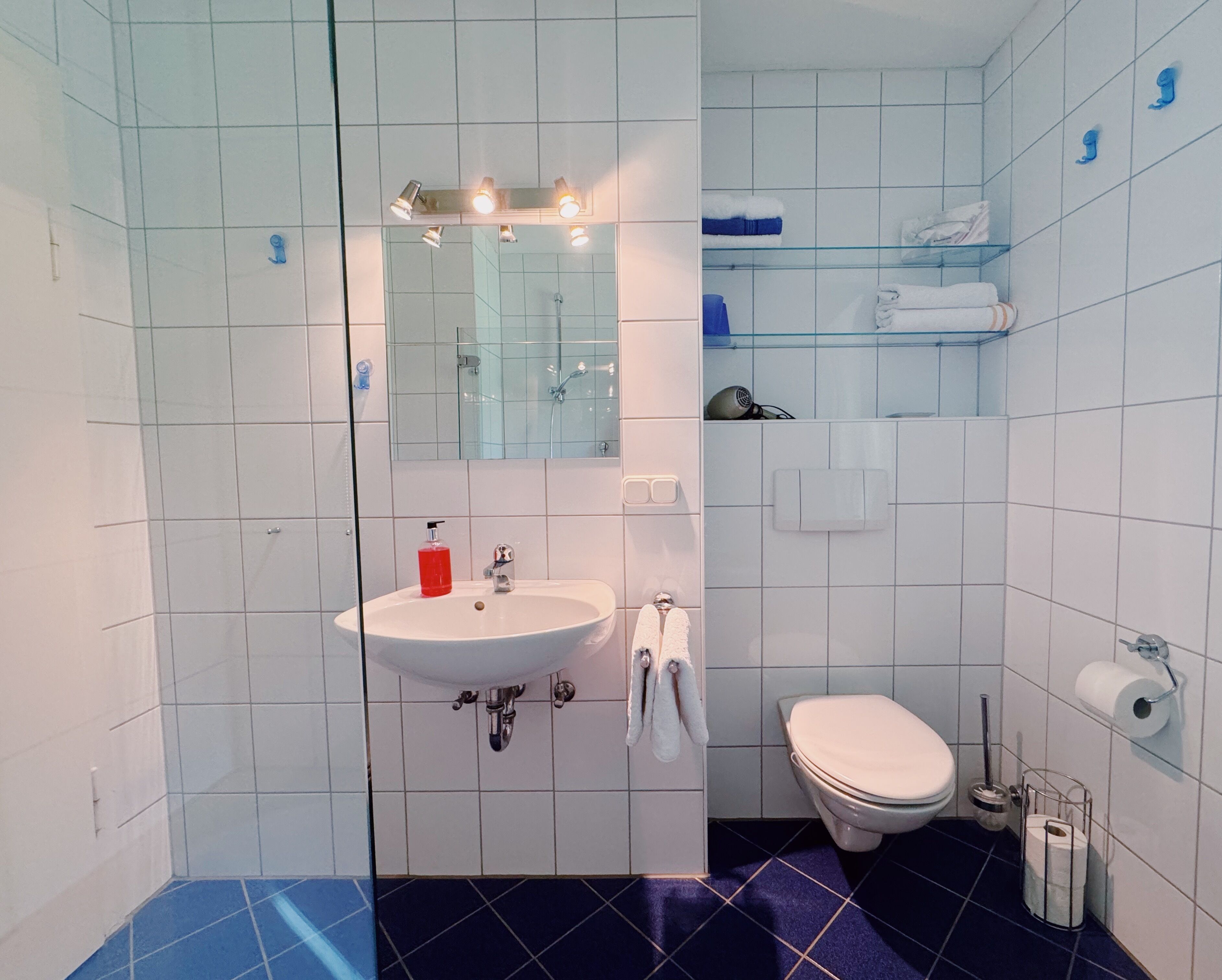 Een badkamer met een wit wastafel, een spiegel, een toilet en een plank met handdoeken.