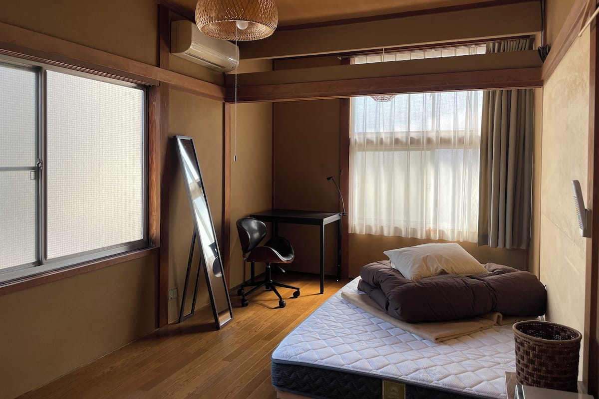 A room with a bed, a desk, a chair, and a large window with curtains.