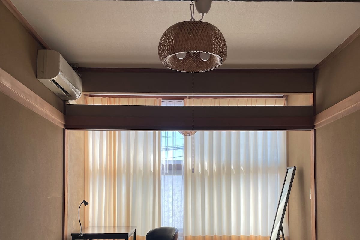 A compact bedroom with a bed, a desk, a chair, and a large window with curtains.