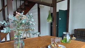 A wooden table with a vase of flowers, plates with food, and a hanging light fixture. - Guesthouse Hayashiya (Omachi)
