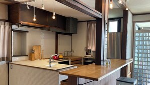 A kitchen with a central island, wooden cabinets, a stainless steel refrigerator, and hanging pendant lights. - Guesthouse Hayashiya (Omachi)