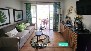 Een woonkamer met een bank, salontafel, televisie en een keukenhoek met aanrecht en fornuis.