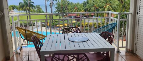 A covered outdoor area with a table and chairs, a view of a pool and palm trees, and a sign reading "Ti Coco Luce".