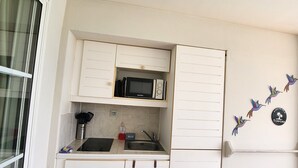 Een kleine keuken met witte kastjes, een magnetron, een spoelbak en een raam.