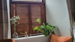 Habitació cantonera amb finestra, una banca amb coixins, una planta en test i un ram de flors.