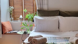 Un llit ben fet amb un edredó verd, dues tovalloles arremolinades i una finestra amb persianes de fusta i plantes.