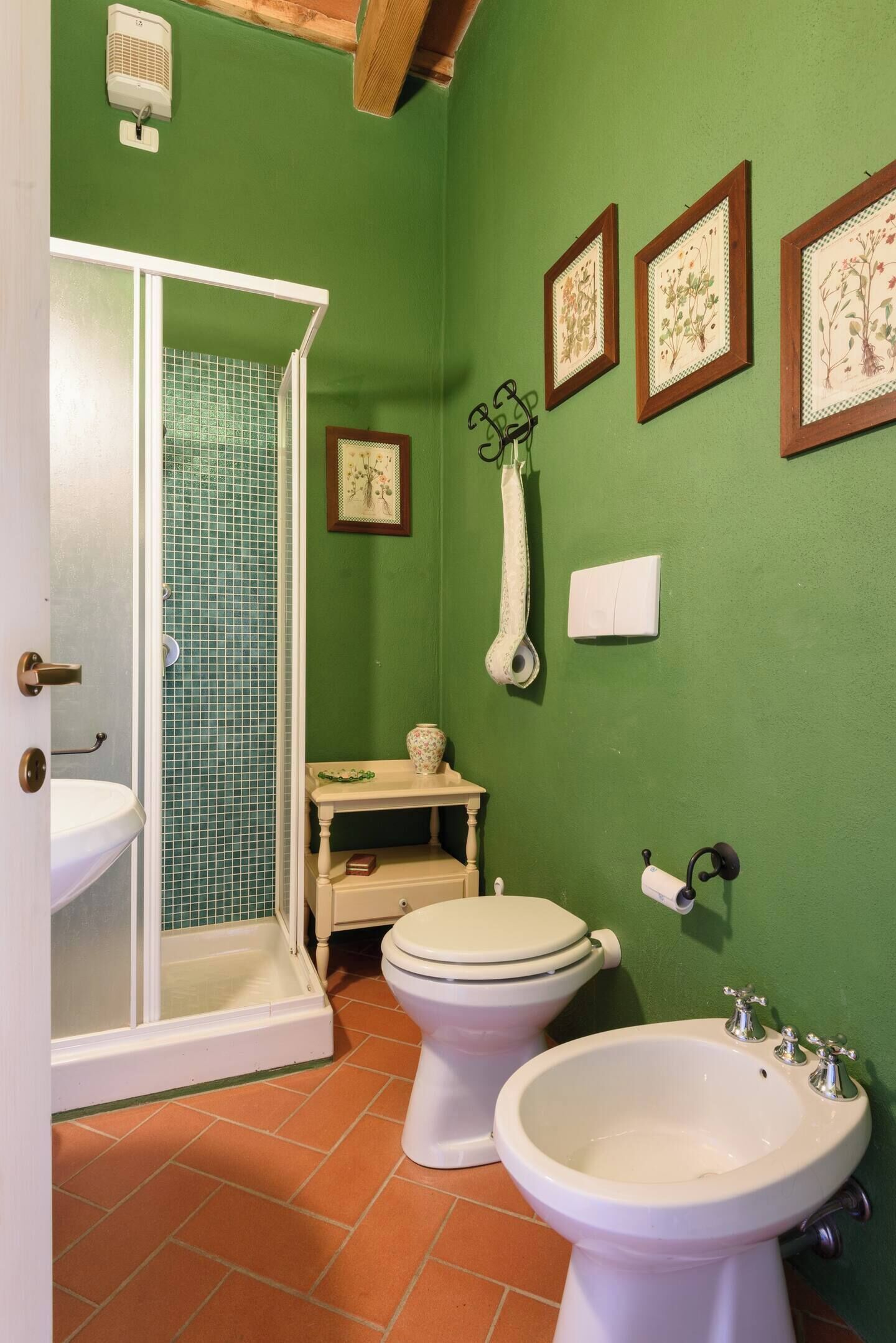 A bathroom with green walls, a white sink, a toilet, a bidet, and a shower enclosure.