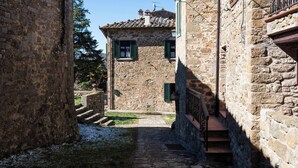 A narrow stone pathway leading to a traditional stone building with a tiled roof and green shutters. - Villa Mille Primavere (Gaiole in Chianti)