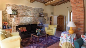 A cozy living room with a stone wall, wooden beams, a black sofa, yellow armchairs, a coffee table, and a patterned rug. - Villa Mille Primavere (Gaiole in Chianti)