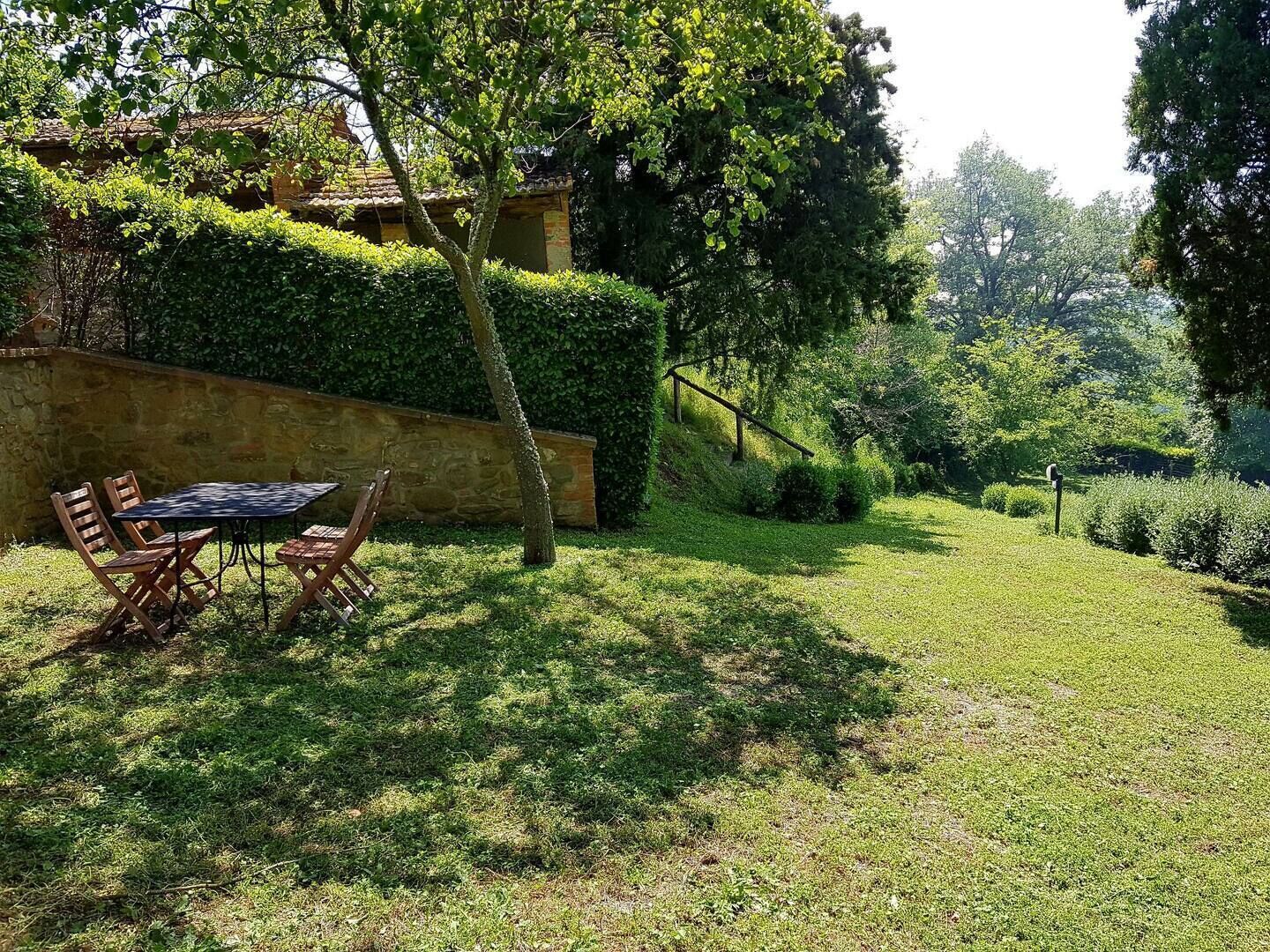 A patio with a table and chairs, surrounded by a well-maintained lawn and a stone wall.