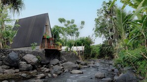 A house with a sloped roof, a stone wall, and a wooden deck. - Camani Glamping (Karangasem)