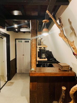 A rustic interior with exposed wooden beams, a wooden counter with a coffee maker, and a hanging light fixture. - Camani Glamping (Karangasem)