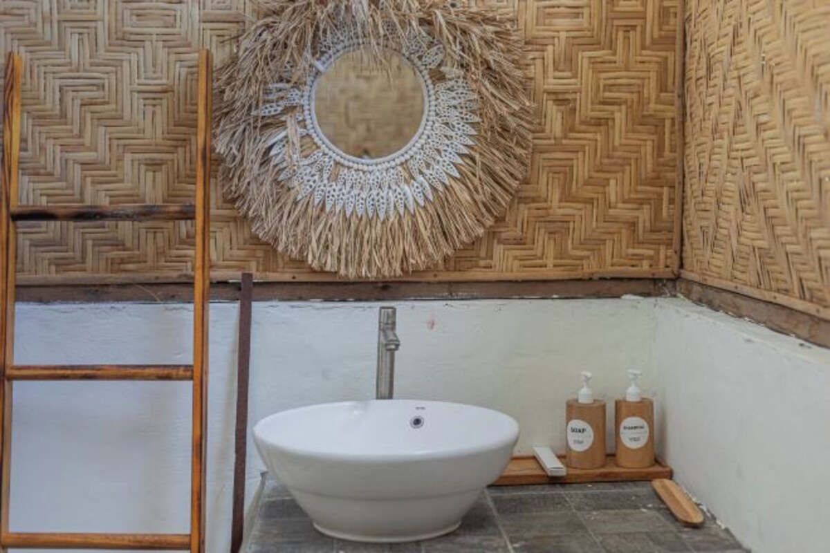 Un baño con un lavabo blanco, una escalera de madera, un tapiz tejido y dos dispensadores de jabón.