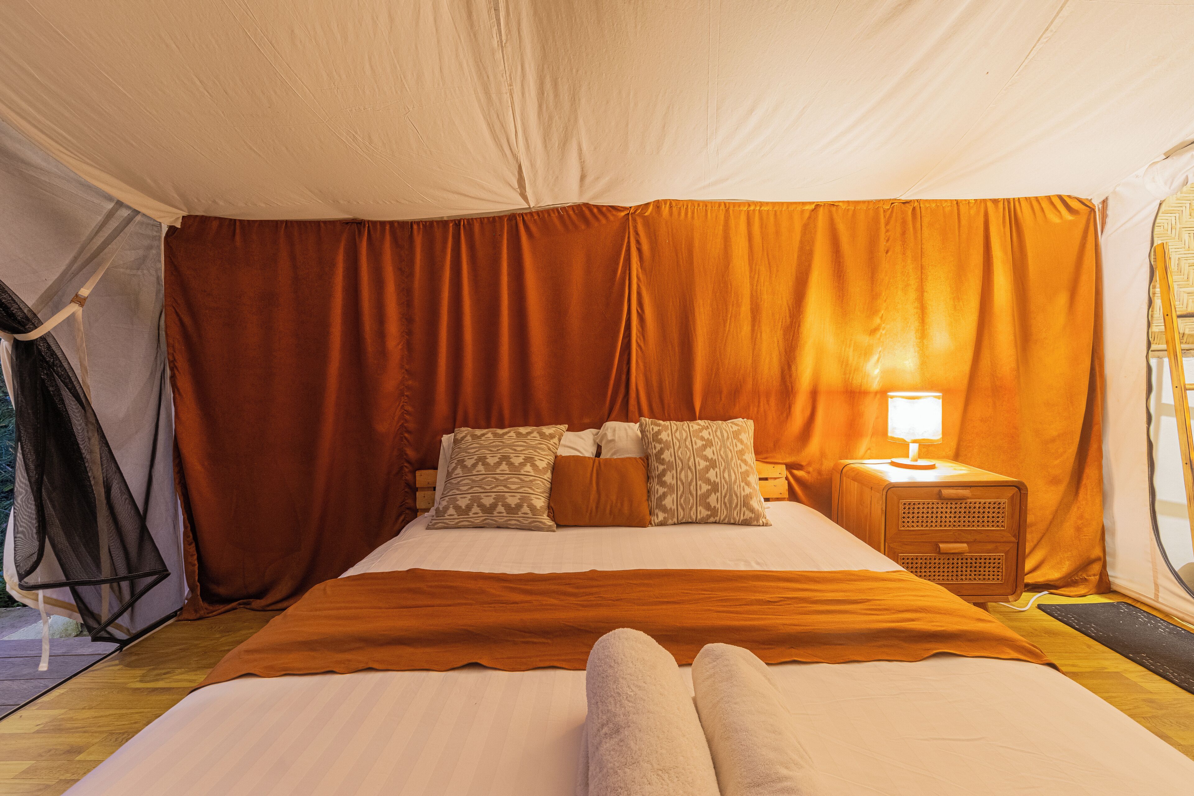 Una habitación con tienda de campaña, una cama, una mesita de noche con lámpara y una ventana con cortinas.