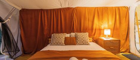 A tented room with a bed, a nightstand with a lamp, and a window with curtains.