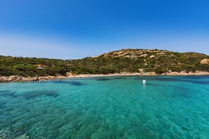 A coastal landscape with clear turquoise waters, a sandy beach, and a hill with sparse vegetation. - Residence I Mirti Apartments (Santa Teresa di Gallura)