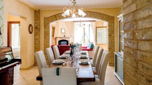 A dining area with a wooden table set for six, surrounded by chairs. A piano is visible to the left, and a fireplace is in the background. - Villa with panoramic pool (Castorano)
