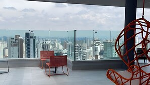 Een moderne kamer met panoramisch uitzicht over de stad, met een rode rieten stoel en een hangstoel.
