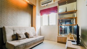 A modern living room with a beige sofa, a flat-screen TV, and a kitchen area visible through a glass partition.