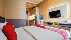 A hotel room with a bed, a desk, a TV, and a kitchenette.