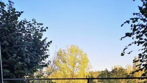 Un balcone con un tavolo di legno e due sedie, circondato da un parapetto in metallo.