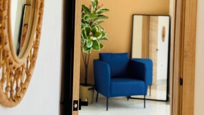 Une porte qui mène à une pièce où se trouvent une chaise bleue, une plante en pot et un miroir au mur.