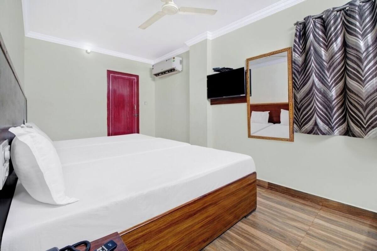 Una habitación de hotel con una cama, una puerta roja, un ventilador de techo, un televisor montado y un espejo.