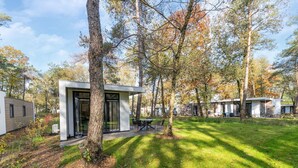 A modern outdoor dining area with a table and chairs, surrounded by trees and a grassy lawn. - Vacation Home in Haarle near Hellendoorn (Haarle)