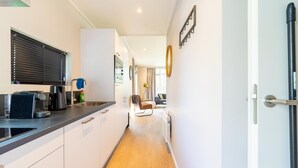 A narrow hallway with a kitchen area on the left, featuring a toaster, coffee maker, and a window with blinds. A door with a handle is visible on the right. - Vacation Home in Haarle near Hellendoorn (Haarle)