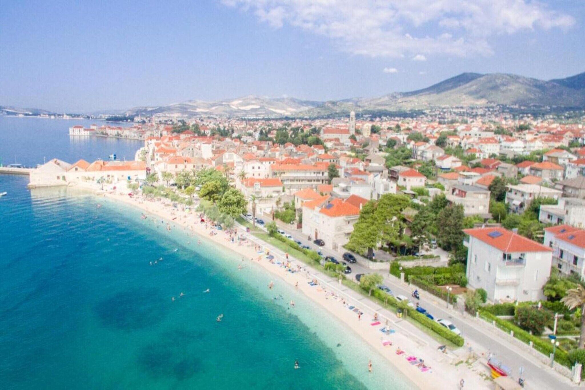 A coastal town with a beach, buildings with red roofs, and a clear blue sea.