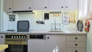 A modern kitchen with stainless steel appliances, a built-in dishwasher, and a variety of utensils hanging on the wall. - Faliron Urban Retreat (Palaio Faliro)
