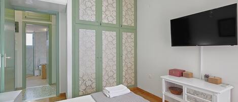 Quarto com cama, televisão, mesa de consola e guarda-roupa com papel de parede estampado.