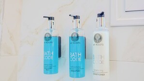 Three bottles of My Roots bath products: energizing hand and body wash, refreshing shampoo, and balancing conditioner, arranged on a marble surface. - Faliron Urban Retreat (Palaio Faliro)