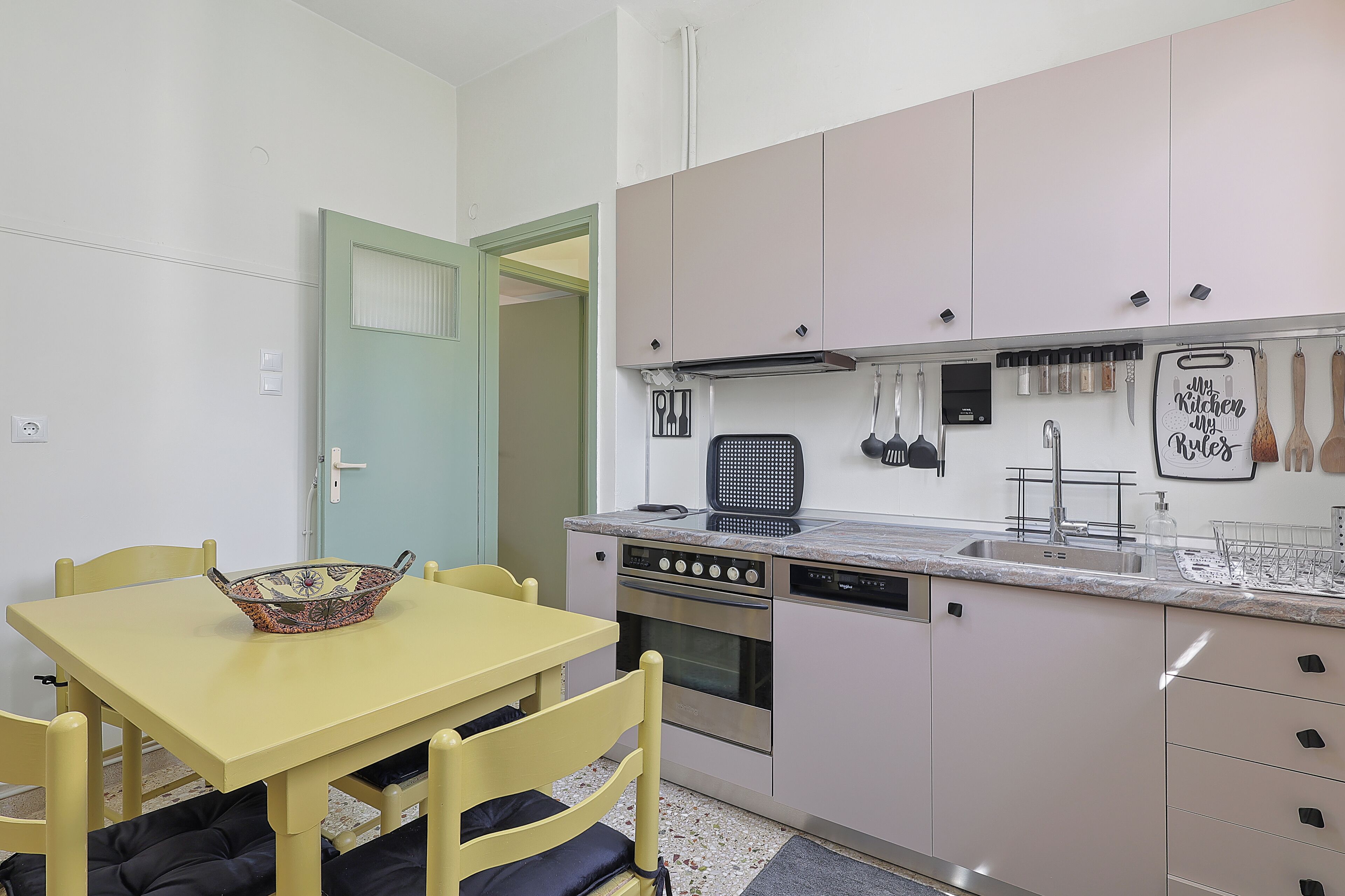 Une cuisine compacte avec une table et des chaises jaunes, un four encastré et un lave-vaisselle.