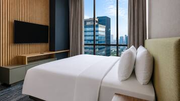 A hotel room with a large bed, a flat-screen TV mounted on the wall, and a city view through the window.