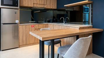 Una cocina moderna con gabinetes de madera, electrodomésticos de acero inoxidable, una mesa de comedor de madera con dos sillas y una lámpara colgante.