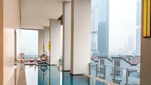Une chambre d’hôtel moderne dotée d’un grand balcon, d’une piscine et offrant une vue sur la ville.