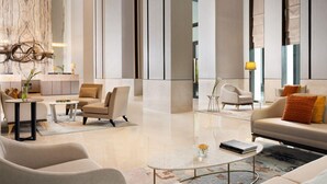 Un hall d’hôtel moderne au design minimaliste, comprenant un espace de détente central avec des canapés et des fauteuils, une table basse et un élément décoratif mural.