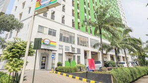 A multi-story building with a GLV Mart sign, a parking area with cars, and a palm tree. - OYO 93948 Bunda Rachma Rooms (Depok)