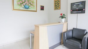 A reception area with a wooden desk, a black leather chair, and a potted plant. - OYO 93948 Bunda Rachma Rooms (Depok)
