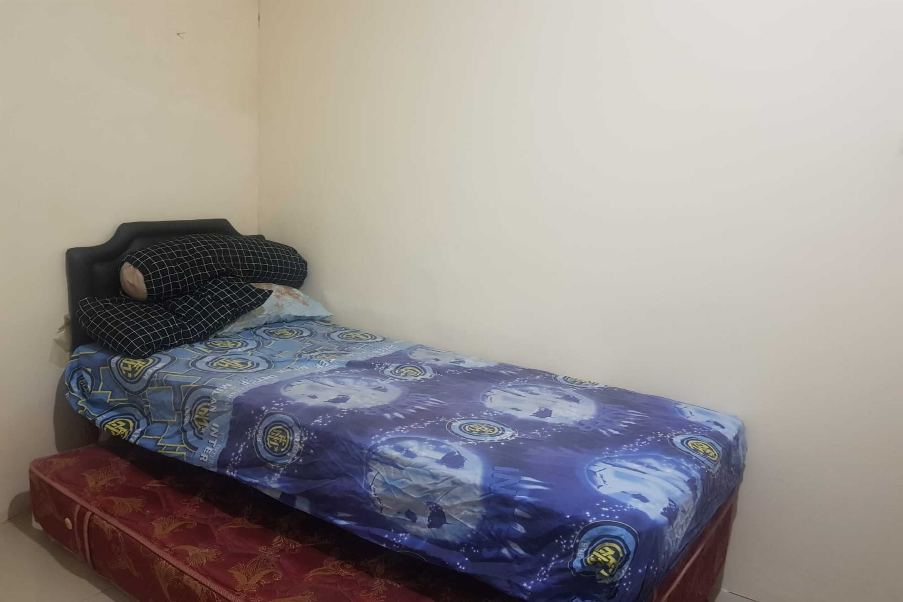 Una habitación pequeña con una cama individual, una colcha estampada y una maleta roja en el suelo.