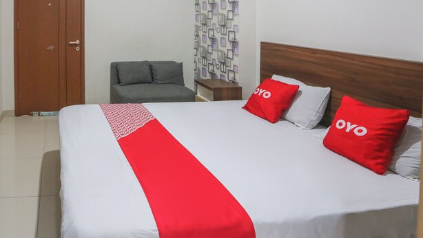 A hotel room with a large bed, two pillows with the word "OYO" on them, a grey sofa, and a wooden headboard. - OYO 93948 Bunda Rachma Rooms (Depok)