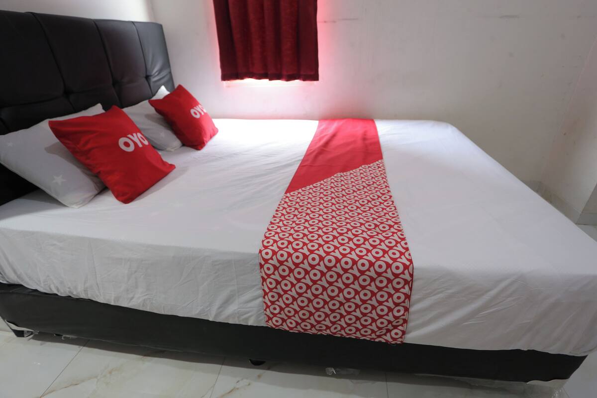 Una cama con una colcha blanca y roja, dos almohadas rojas con la marca 'OYO' y un cabecero negro.