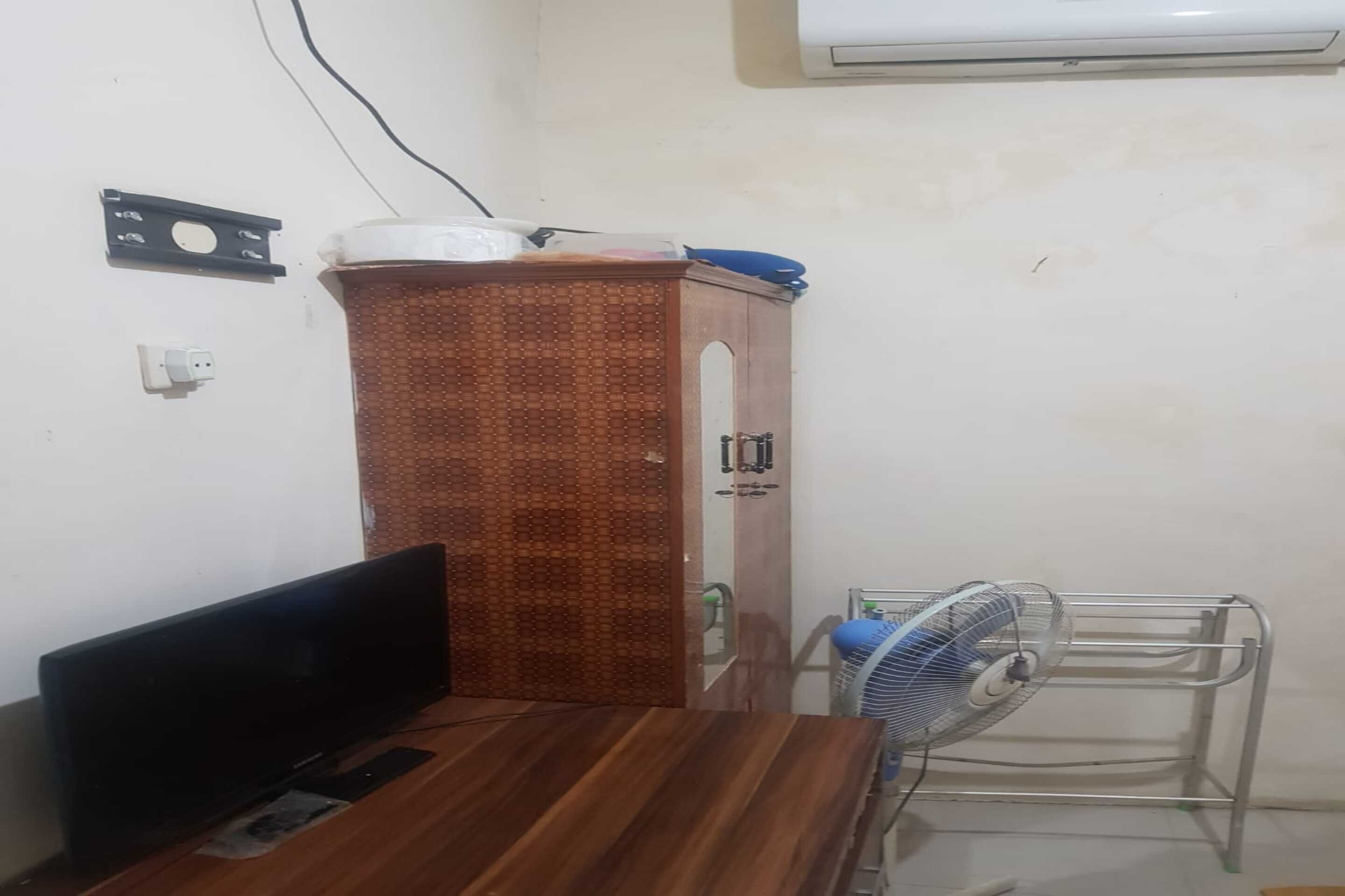 A room with a wooden cabinet, a TV, and a standing fan.