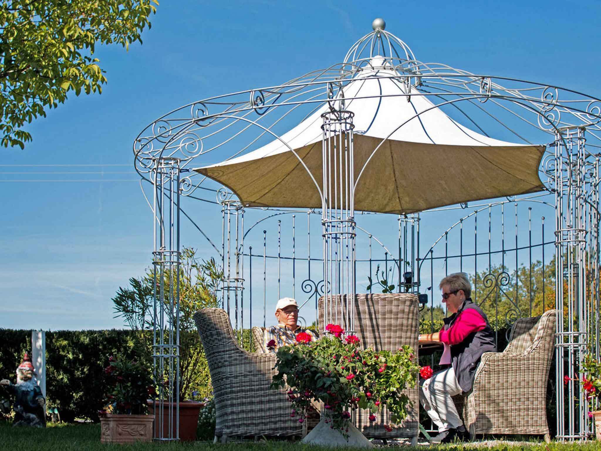 A gazebo with a dome and open sides, surrounded by wicker furniture and potted plants.
