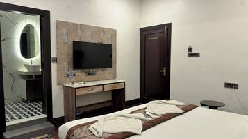 A modern hotel room with a large bed, a TV mounted on the wall, a wooden wardrobe, and a bathroom with a marble vanity.