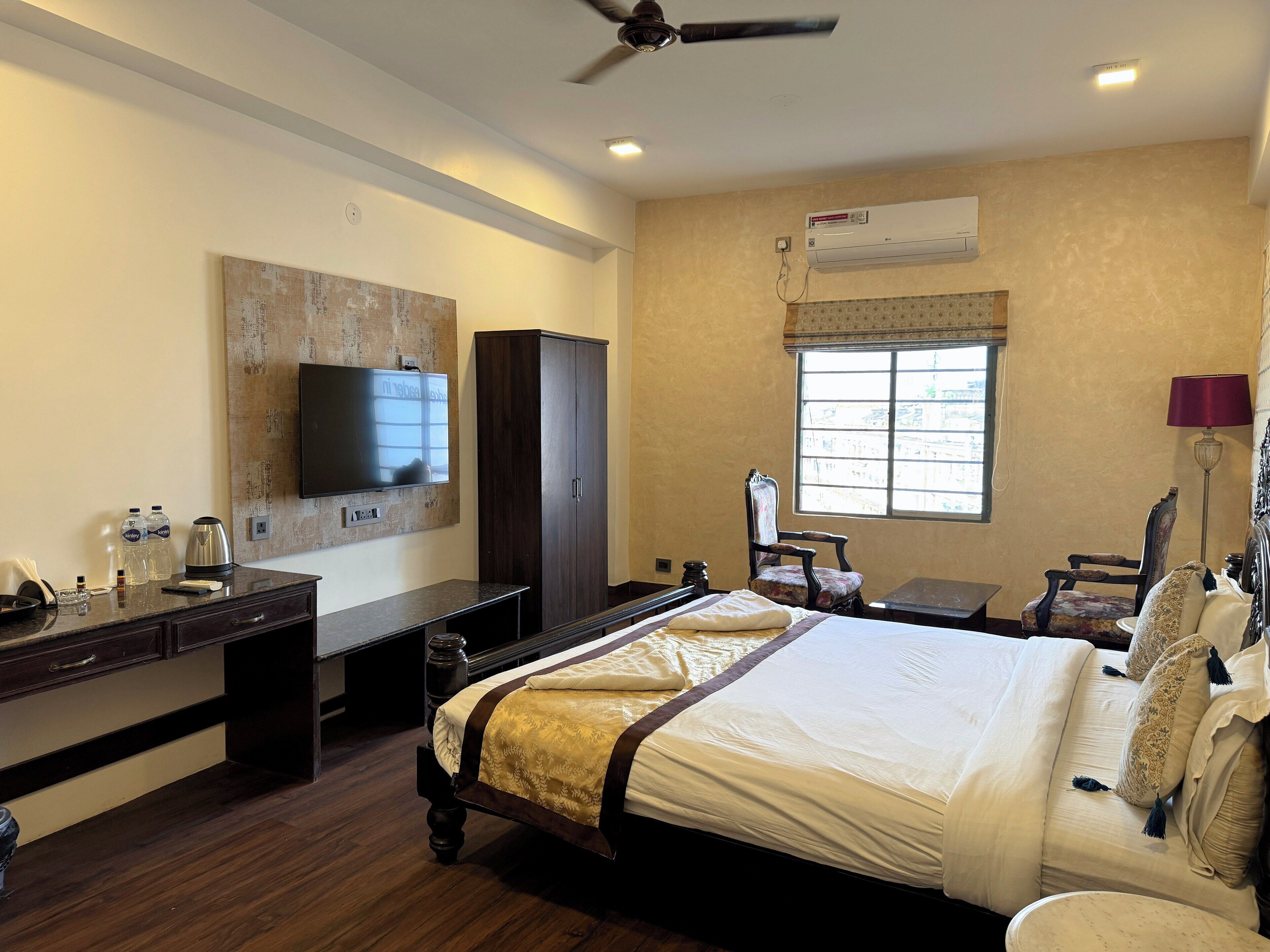 A hotel room with a bed, a desk, a wardrobe, a television, and an air conditioning unit.