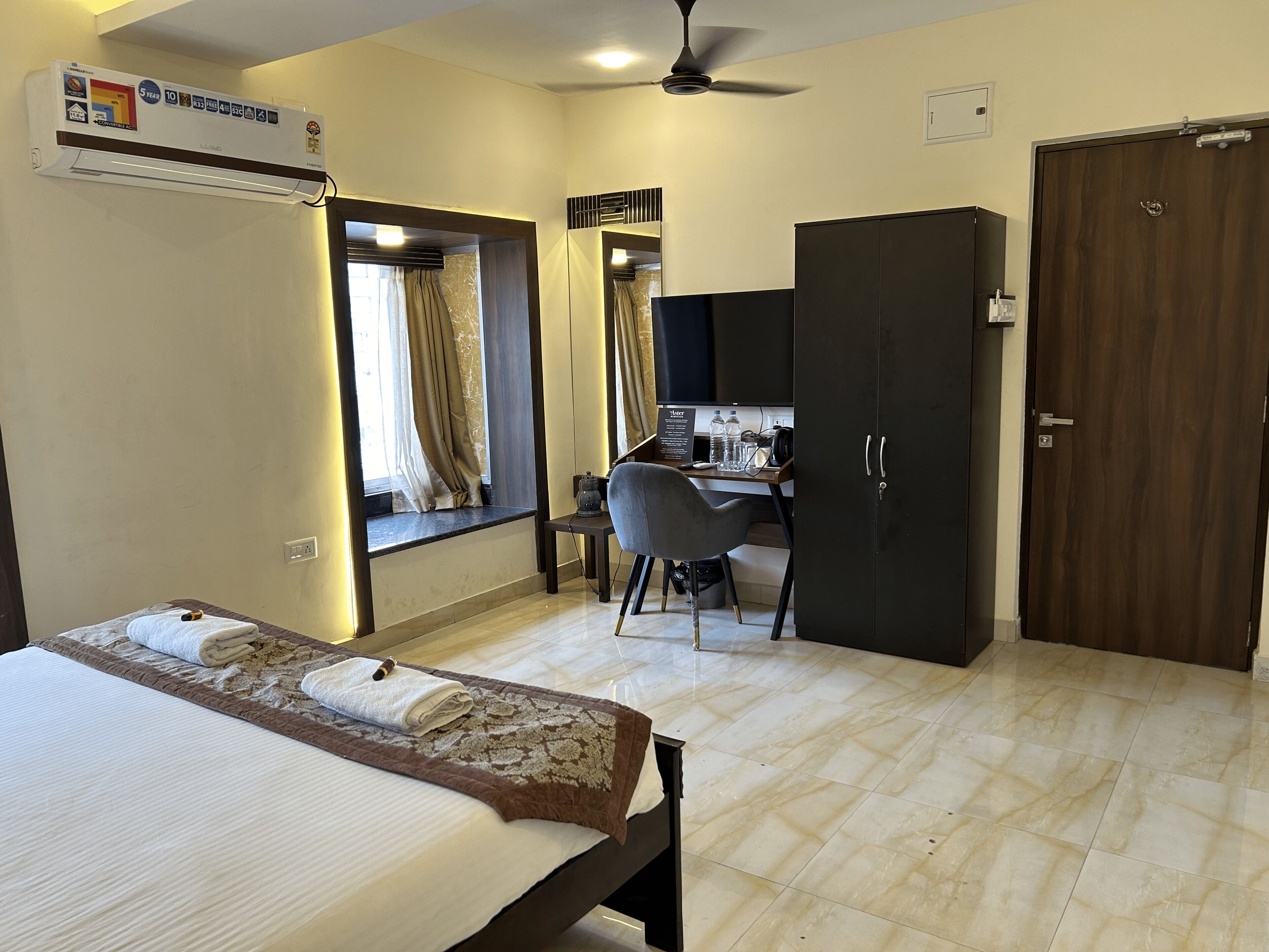 A hotel room with a bed, a desk, a wardrobe, and a ceiling fan.
