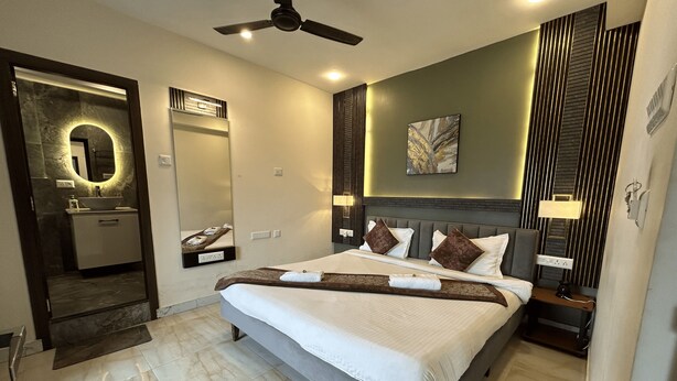 A modern hotel room with a large bed, a ceiling fan, a bathroom with a vanity, and a large mirror. - The Aster Heritage (Kolkata)